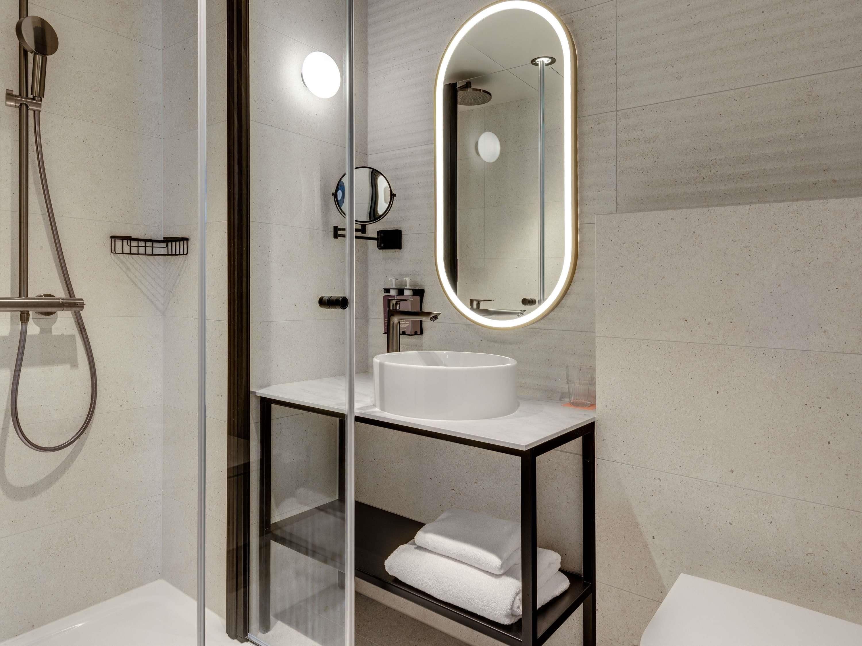 Une salle de bain moderne avec une douche en verre, un lavabo blanc, un miroir avec éclairage intégré et un porte-serviettes.