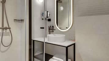 Une salle de bain moderne avec une douche en verre, un lavabo blanc, un miroir avec éclairage intégré et un porte-serviettes.