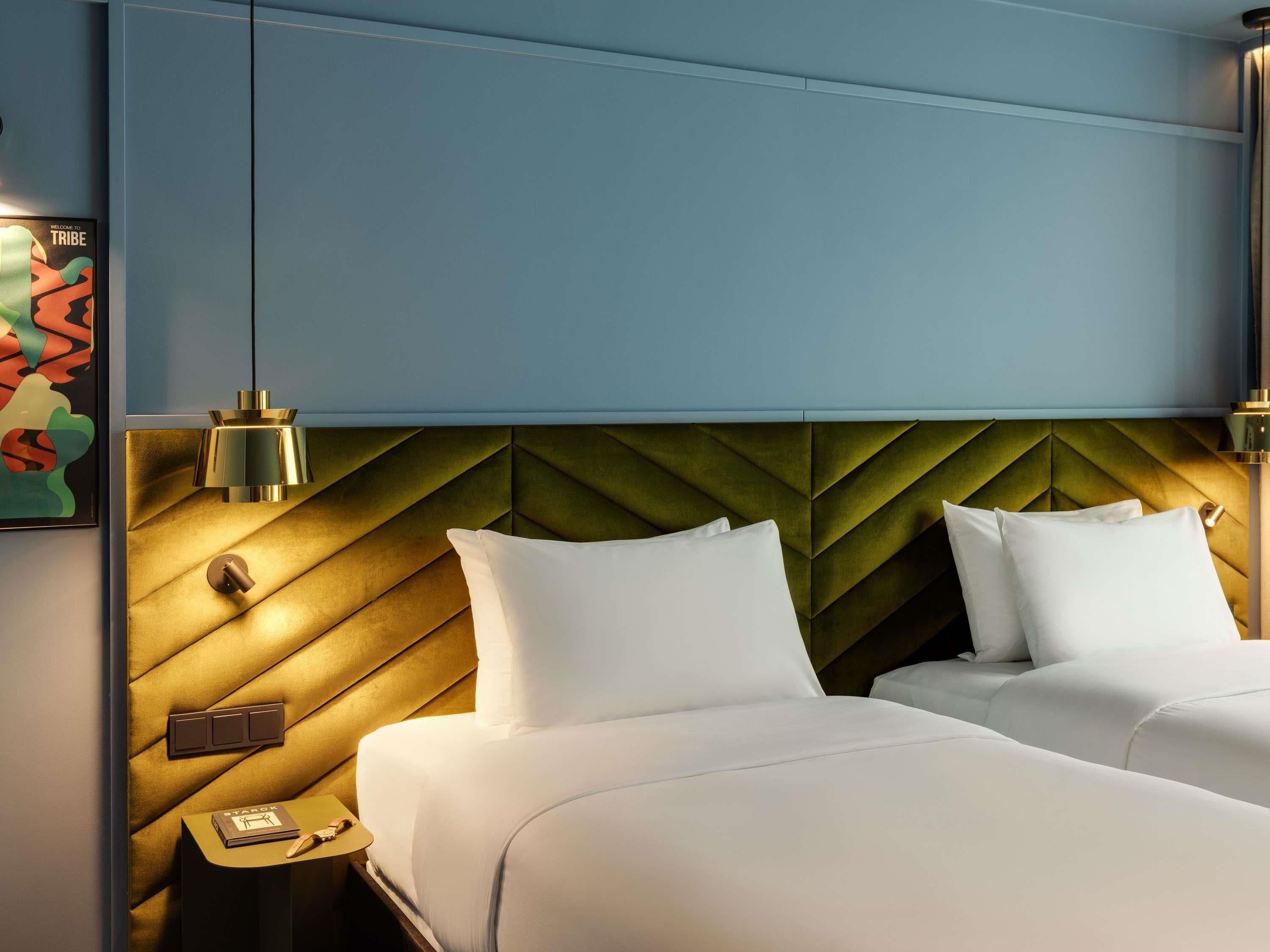 Een hotelkamer met twee bedden, een groen hoofdeinde, bedlampen, een nachtkastje met een telefoon en een aan de muur hangend kunstwerk.