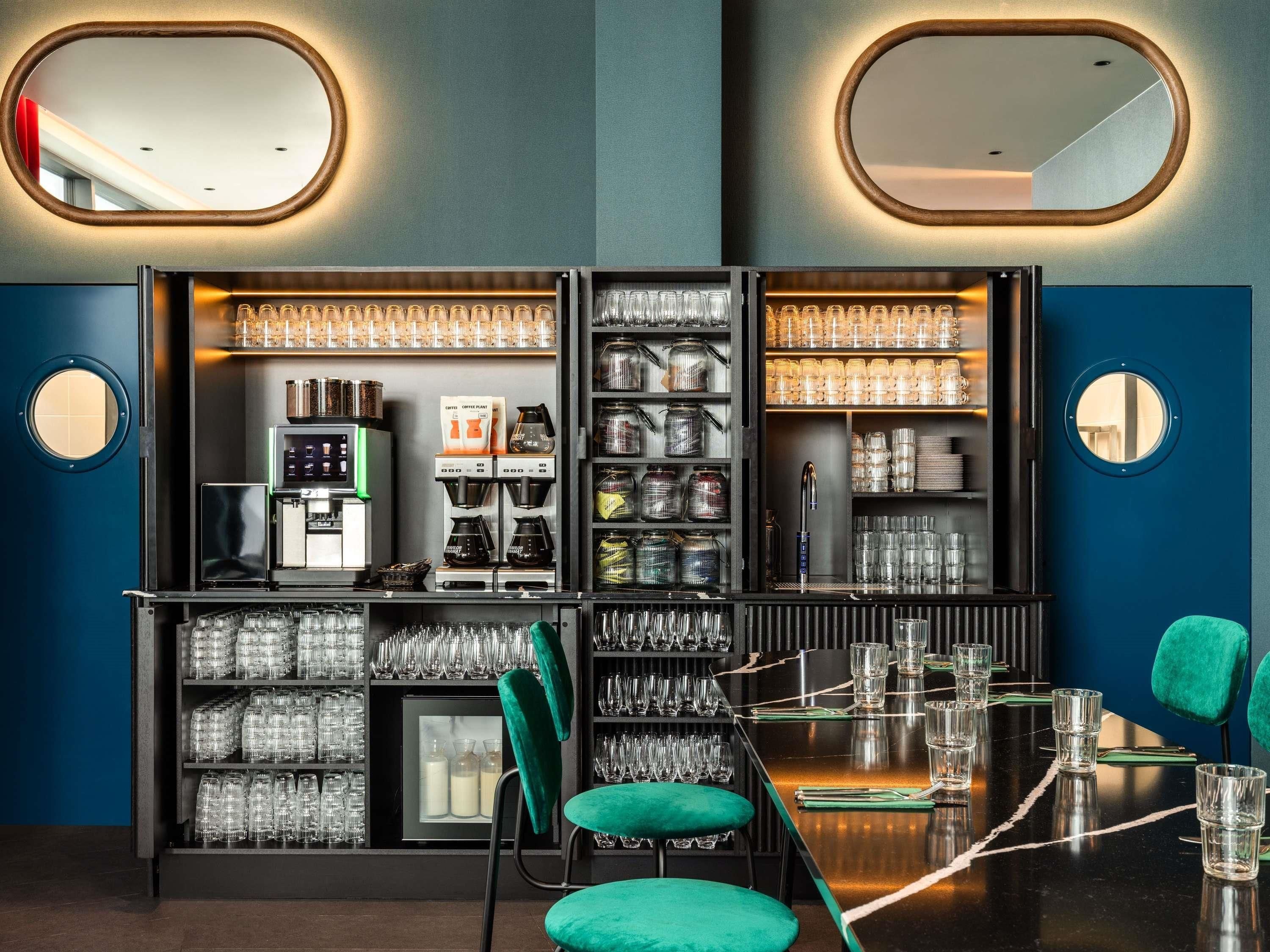 Una zona de bar con una máquina de café, estantes llenos de vasos y un espejo.