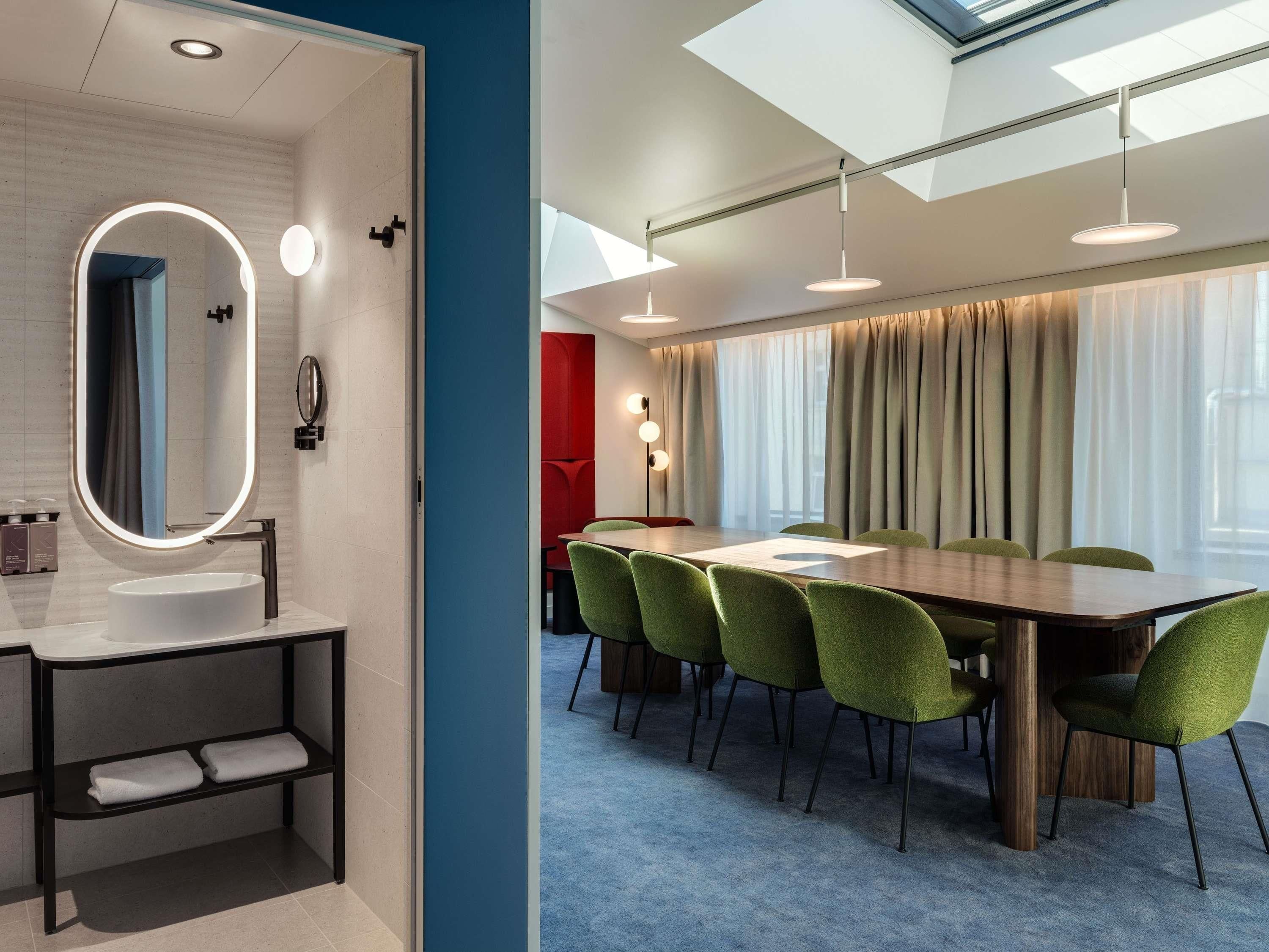 A modern hotel room with a bathroom, a dining area with a table and chairs, and a large window with curtains.