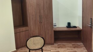 Une pièce comprenant une armoire en bois, un fauteuil en rotin, une petite table avec deux bouteilles et une machine à café.