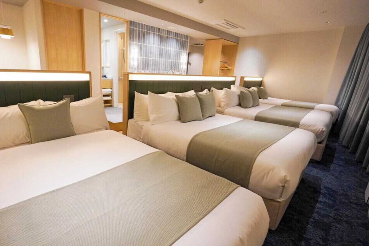 Habitación de hotel con tres camas, un espejo grande y vistas a un balcón.