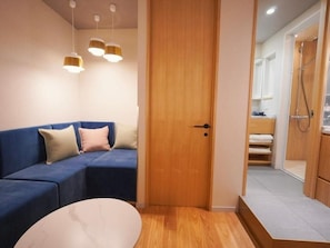Ein Zimmer mit einem blauen Sofa, einer Holztür und einem Duschbereich.