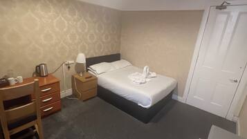 A hotel room with a bed, a desk, a chair, a nightstand, a lamp, a coffee maker, and a wardrobe.