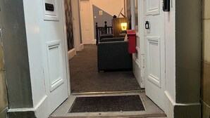 A hallway with a carpeted floor, a doormat, a staircase, and a door with a caution sign. - Piccolo Hotel (Glasgow)