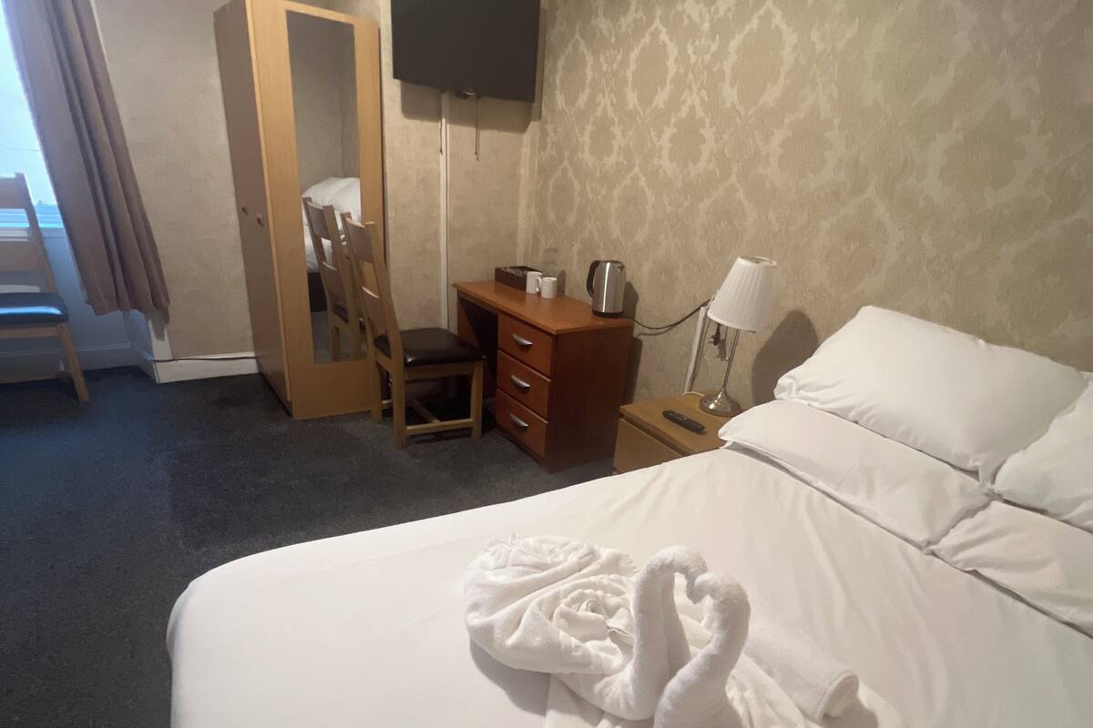 A hotel room with a bed, a desk, a chair, a television, and a lamp.