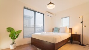 A modern bedroom with a large bed, a potted plant, and a bedside table with a lamp. - Travel Time Sumiyoshi Suzaku (Osaka)