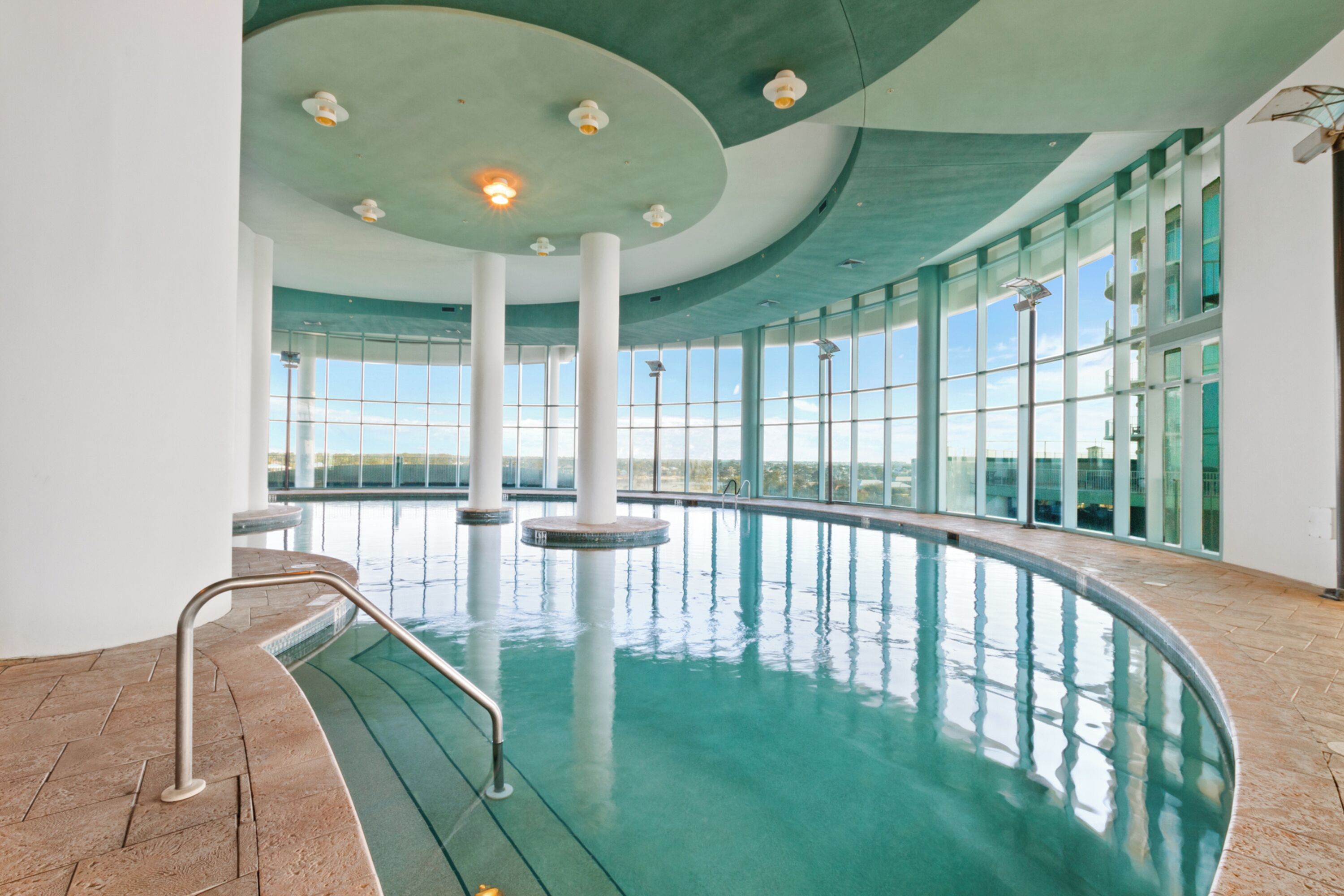 An indoor swimming pool with clear glass walls, a curved ceiling, and a herringbone-patterned floor.