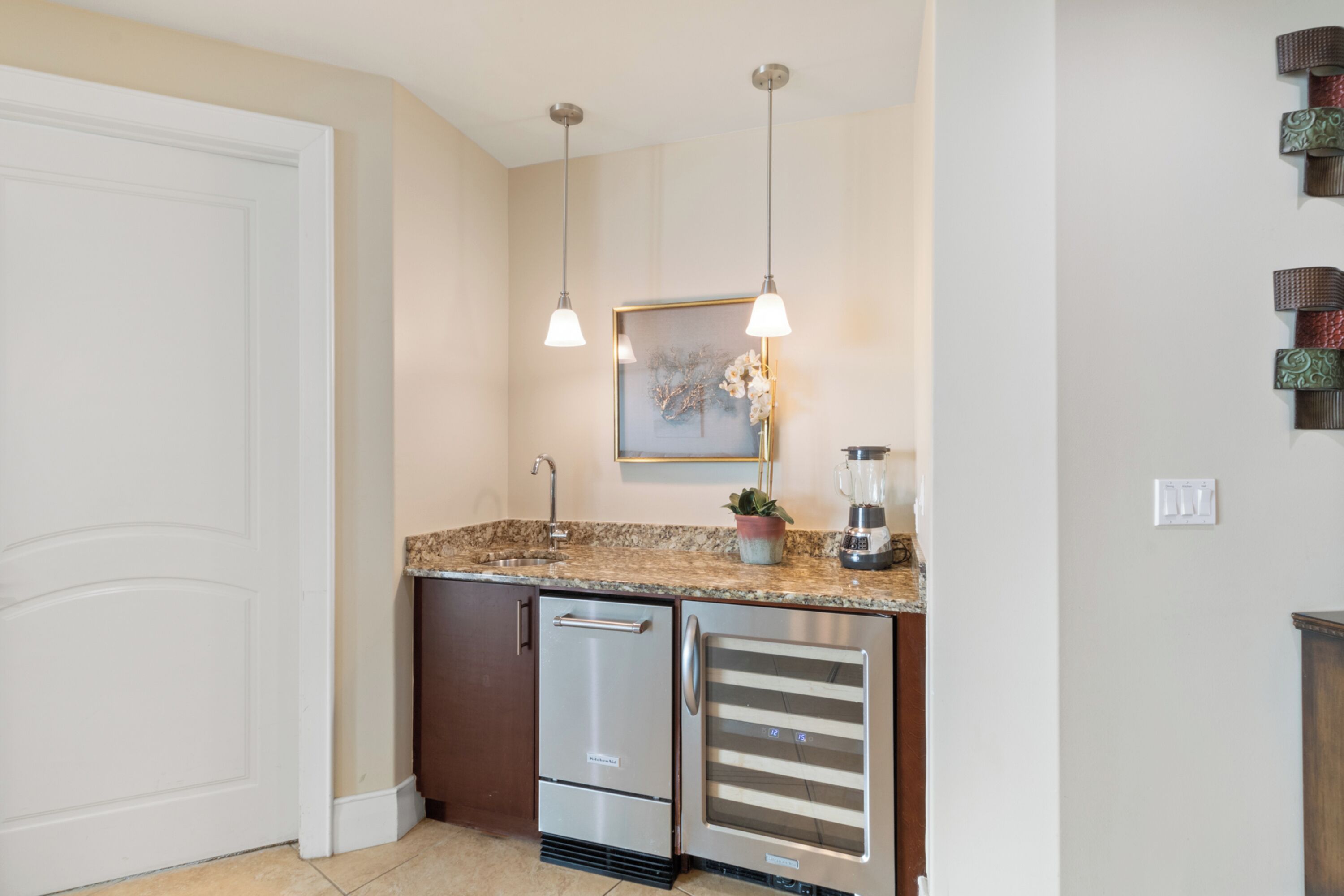 A kitchen with stainless steel appliances, a granite countertop, pendant lighting, and a framed artwork above the sink.