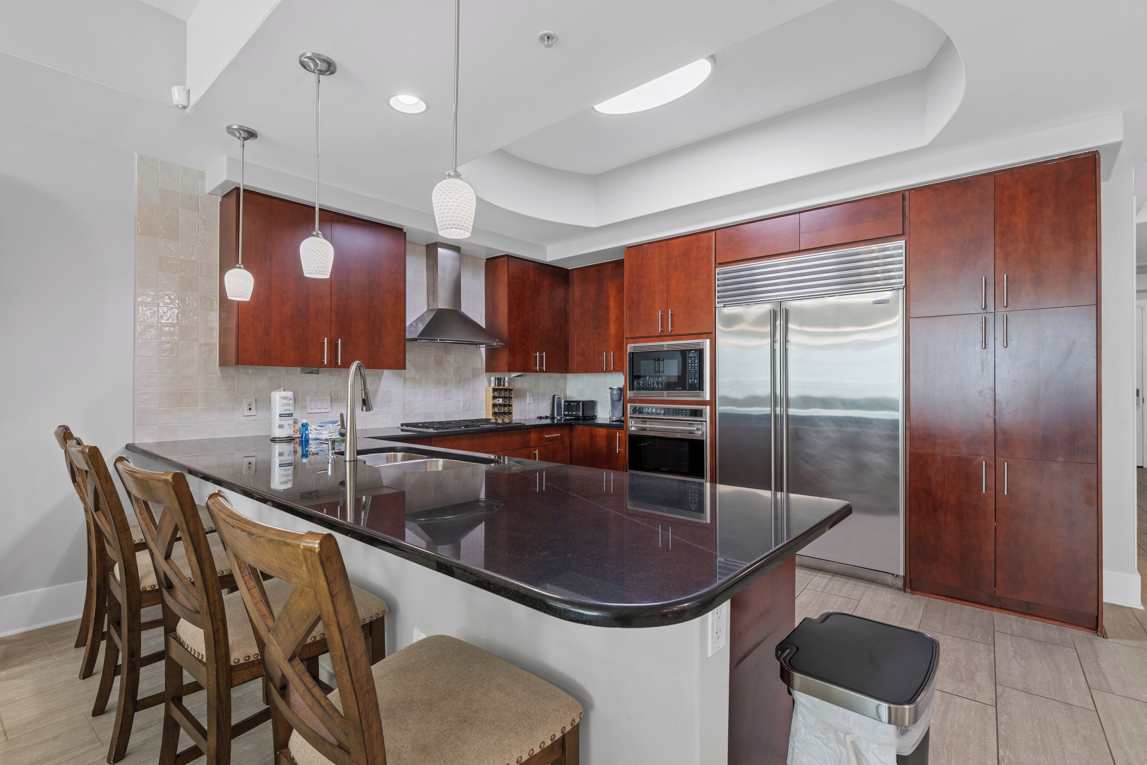 A modern kitchen with a central island, stainless steel appliances, wooden cabinets, and pendant lighting.