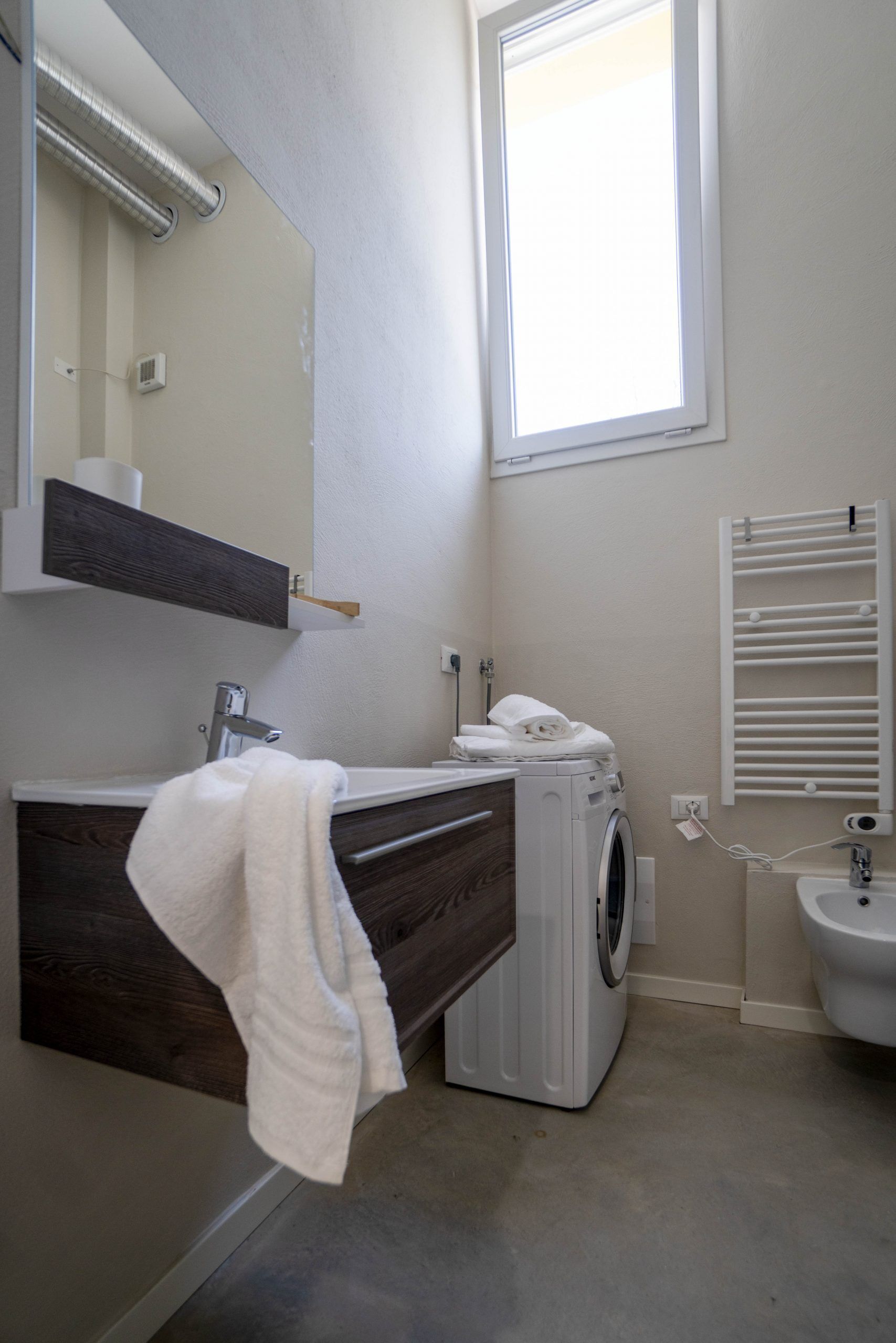 A modern bathroom with a built-in washing machine, a sink, a towel rack, and a window providing natural light.