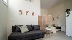 A modern living room with a dark grey sofa, a small round rug, and a wooden partition with a plant. - 3 Lofts for 9 People, Abete 3p, Noce 4p, Rovere 2p (Castel San Pietro Terme)