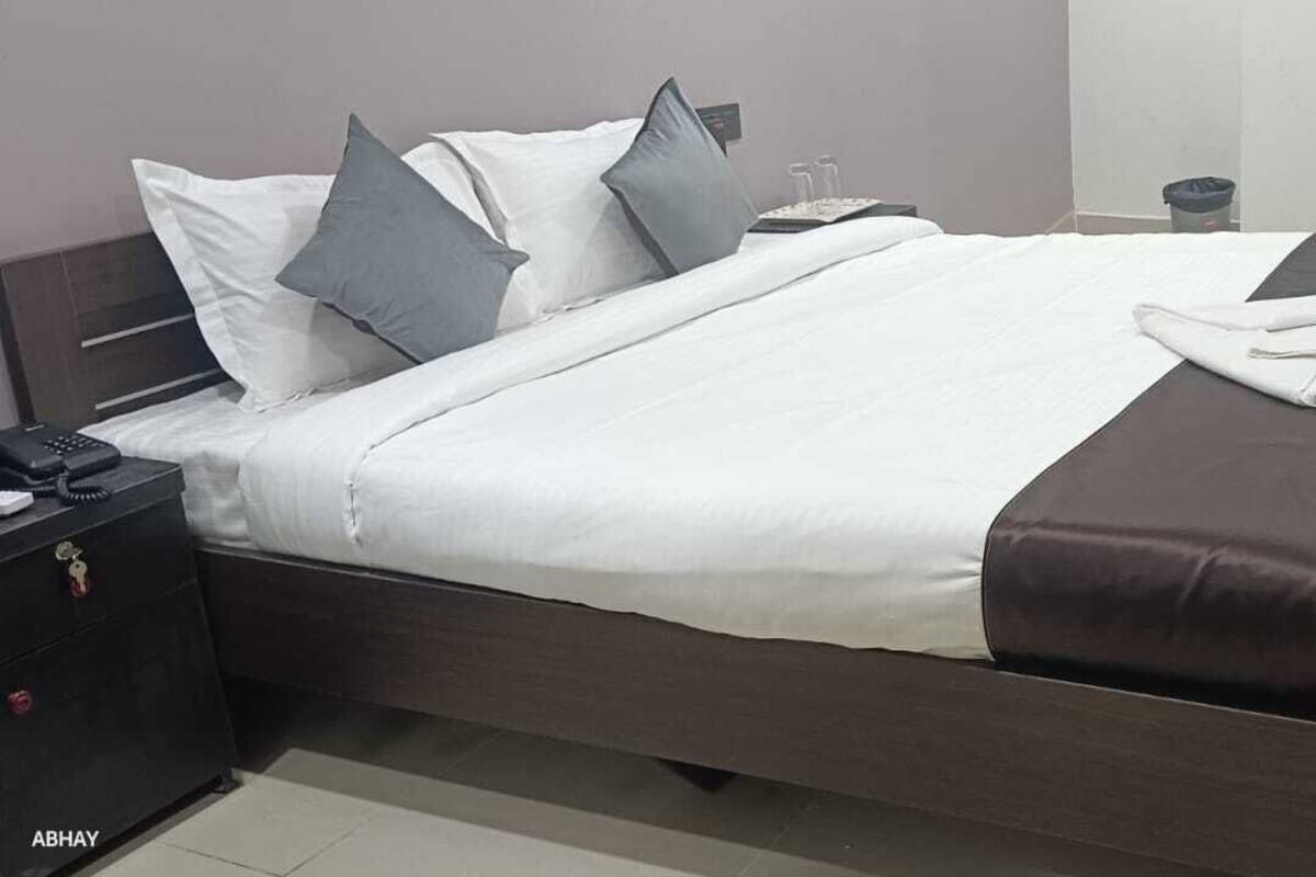 Una cama bien hecha con ropa de cama blanca y gris, una almohada de acento marrón oscuro y una manta marrón.