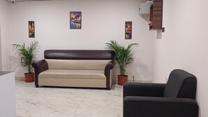 A living room with a beige sofa, a dark armchair, two potted plants, and three framed pictures on the wall. - HOTEL BLACK GRAPES INN (Bhubaneshwar)