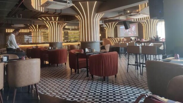 A modern restaurant interior with a checkered floor, red upholstered chairs, and a bar area with a screen. - HOTEL BLACK GRAPES INN (Bhubaneshwar)