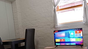 Un salon avec un téléviseur posé sur un meuble en bois, une table à manger avec des chaises et une fenêtre avec des rideaux.