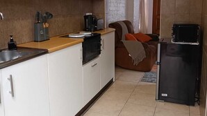 Une cuisine de taille réduite avec des meubles blancs, un réfrigérateur noir et une machine à café.