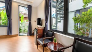 A modern hotel room with a wooden floor, a dining table with chairs, a TV, and a view of a building with a staircase. - Private Beachfront House 5BRs - An Bang Beach (Thành phố Hội An)