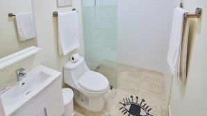 A bathroom with a sink, toilet, and shower. There are towels hanging on the wall and a glass shower door. - Modern Santo Domingo Condo in Heart of Gazcue (Santo Domingo)