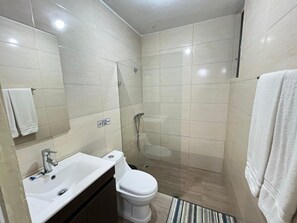 A compact bathroom with a sink, toilet, and glass-enclosed shower. - Modern Santo Domingo Condo in Heart of Gazcue (Santo Domingo)