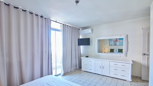 A hotel room with a bed, a TV, a dresser, and a window with curtains. - Modern Santo Domingo Condo in Heart of Gazcue (Santo Domingo)