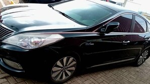 Un sedán negro estacionado sobre una superficie pavimentada.