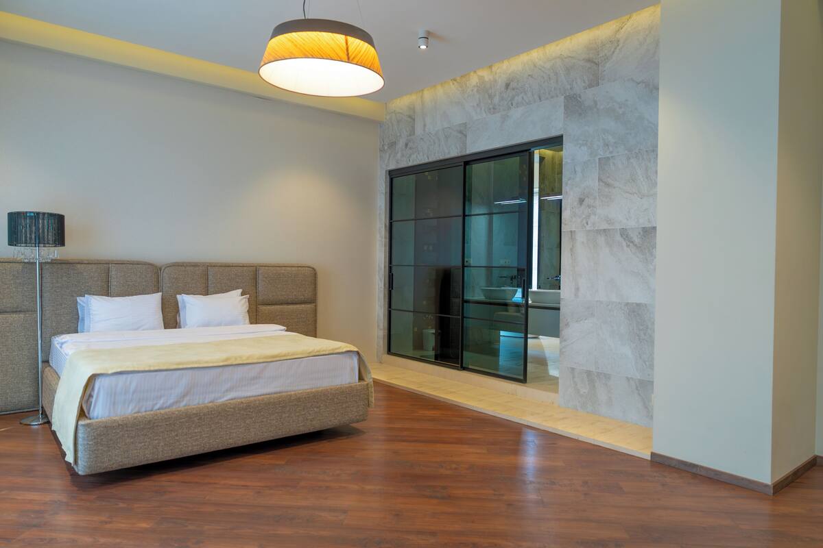 A modern bedroom with a large bed, a floor lamp, and a glass wall.