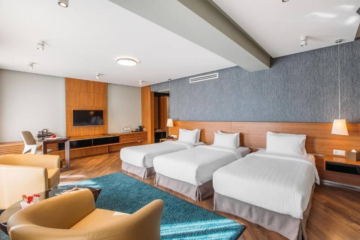 A hotel room with three beds, a TV, a desk, and a seating area.