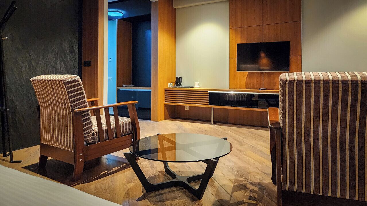 A modern living room with striped armchairs, a glass coffee table, and a flat-screen TV mounted on the wall.