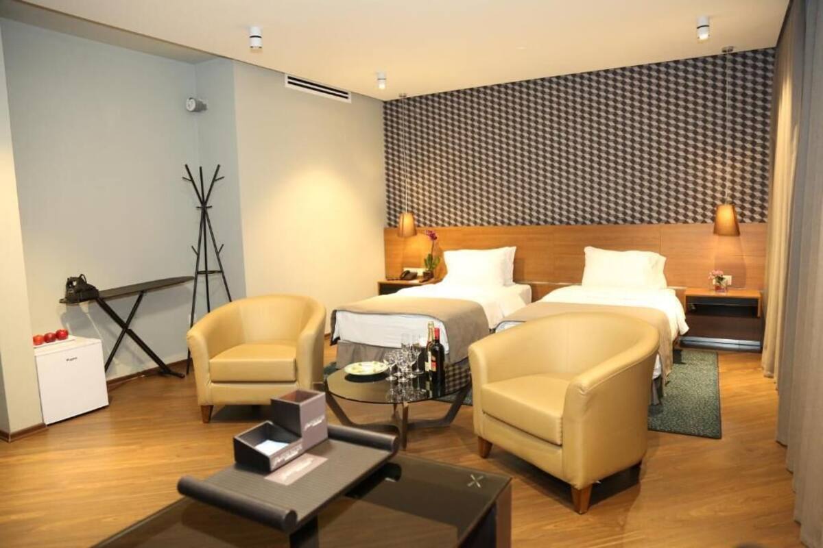 A hotel room with two beds, a sofa, a coffee table, and a coat rack.
