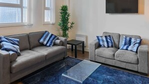 Ein Wohnzimmer mit zwei Sofas, einem Couchtisch, einer Topfpflanze und einem flachbildfernseher an der Wand.