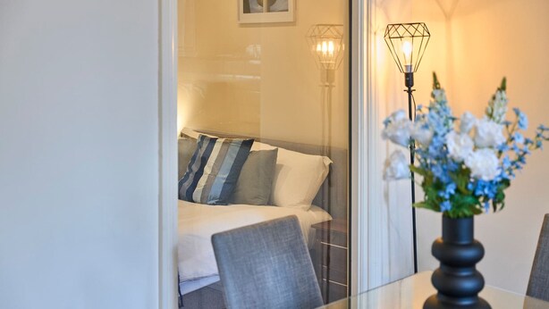 Ein Hotelzimmer mit einem Bett, einem Sessel, einem Tisch mit Blumen in einer Vase und zwei Wandlampen.