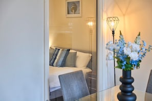 A hotel room with a bed, a chair, a table with a vase of flowers, and two wall-mounted lamps. - Host Stay Three Graces Getaway (Liverpool)