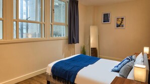 Ein Hotelzimmer mit Bett, Nachttisch, Lampe, Spiegel und einem Fenster mit Vorhängen.