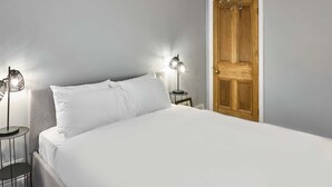 A neatly made bed with white linens, two bedside tables with lamps, and a wooden door. - Host Stay Railway Cottages (Liverpool)