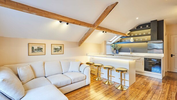 Un loft moderne avec un plafond en bois, un canapé blanc, une cuisine avec un bar et deux tableaux encadrés au mur.
