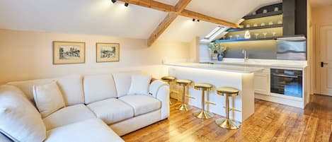 A modern loft with a wooden ceiling, a white sofa, a kitchen with a bar, and two framed pictures on the wall.