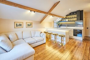 A modern loft with a wooden ceiling, a white sofa, a kitchen with a bar, and two framed pictures on the wall. - Host Stay The Rooftop Gallery (Newcastle-upon-Tyne)