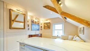 Une pièce spacieuse dotée d’un grand comptoir en marbre blanc, de poutres en bois au plafond et d’un lit recouvert de linge de lit blanc.