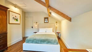 Une chambre avec un grand lit, des poutres apparentes, une commode et des œuvres d’art encadrées accrochées au mur.