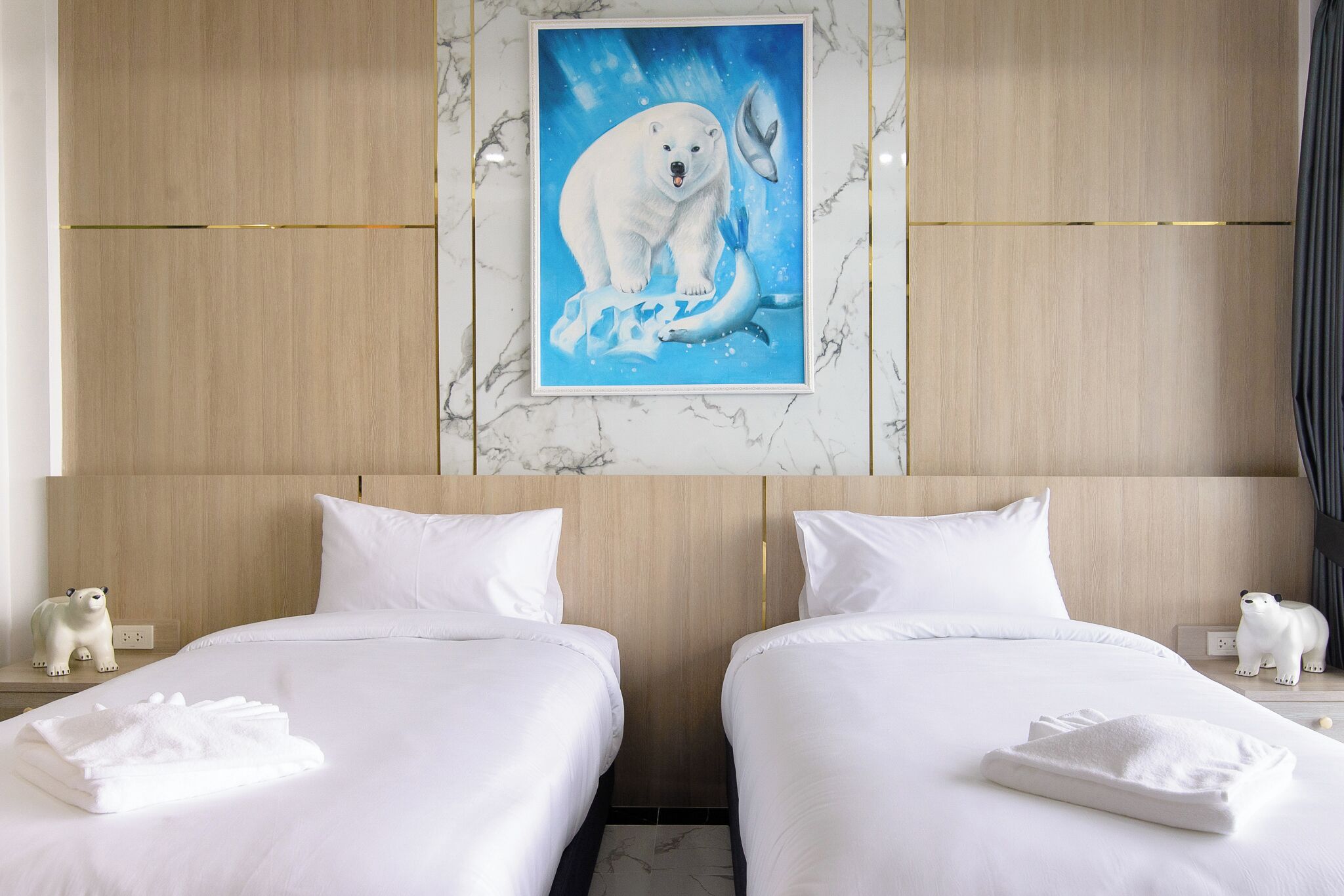 Une chambre d’hôtel avec deux lits, du linge de lit blanc, une statue d’ours polaire sur le côté gauche et un tableau encadré représentant un ours polaire et une baleine accroché au mur.