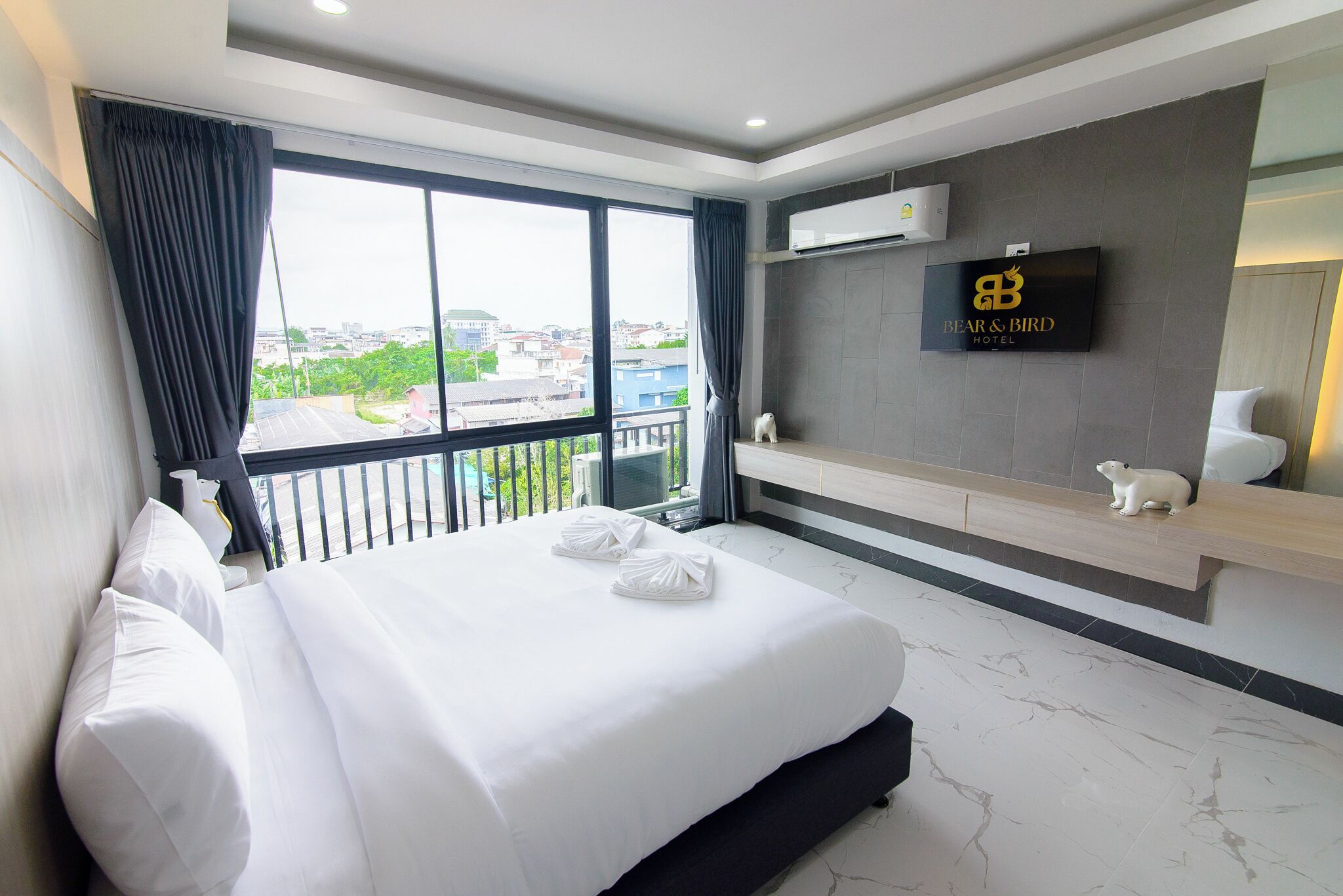 A hotel room with a large bed, a TV mounted on the wall, and a view of the city through the window.