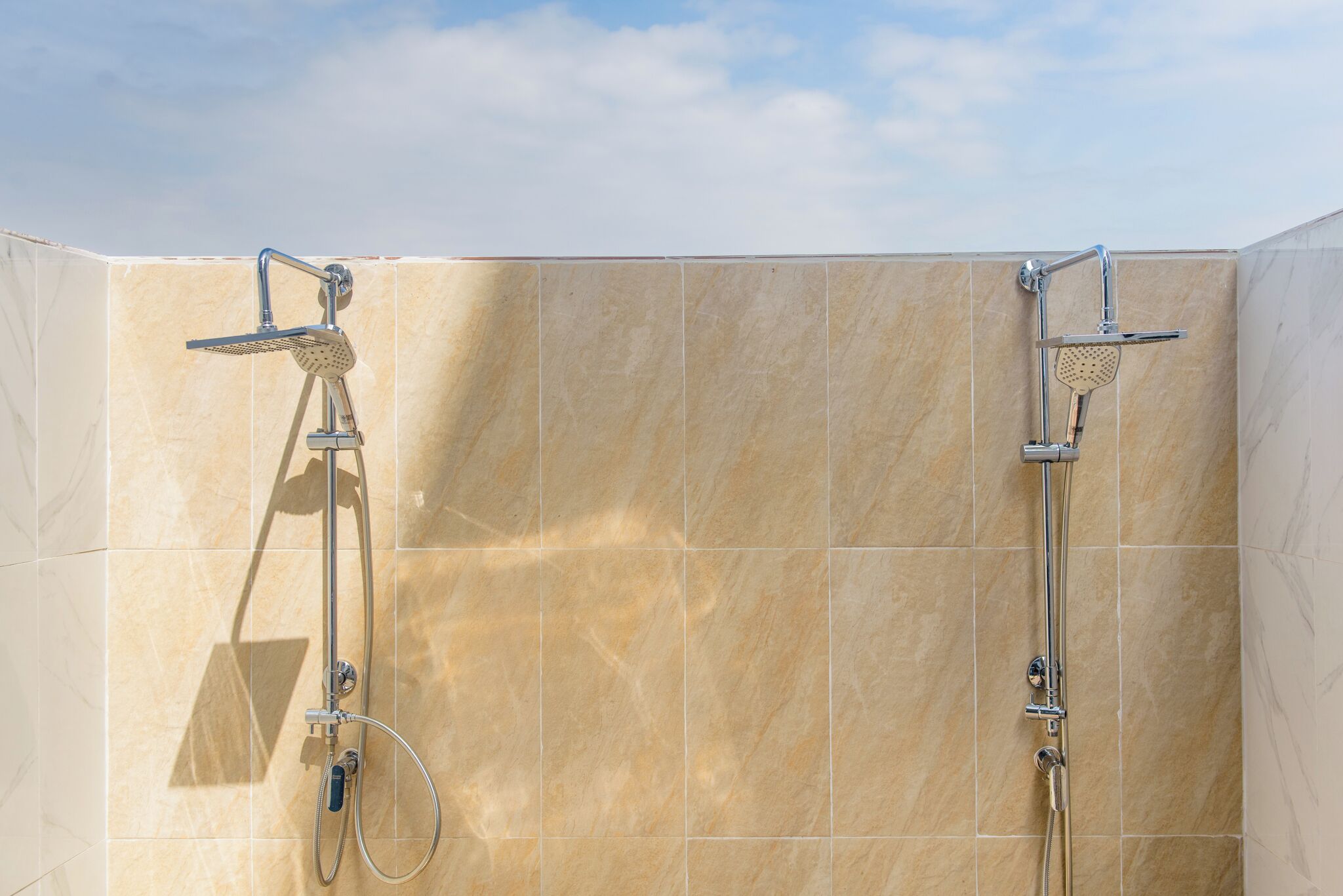 A shower area with two chrome showerheads and a handheld shower attachment.