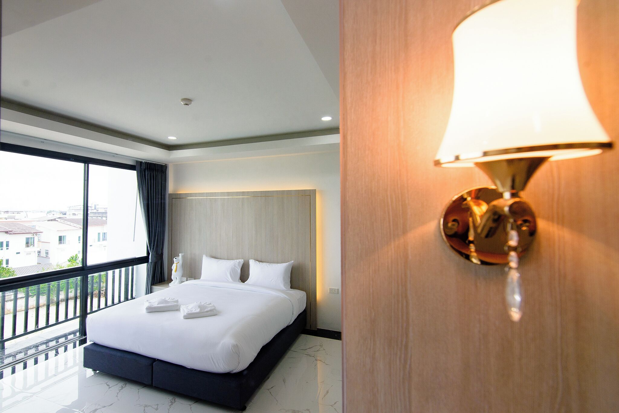 A hotel room with a large bed, a balcony, and a wall-mounted lamp.