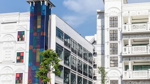 A modern building with a colorful glass tower and traditional white facades with balconies. - Bear & Bird Hotel   (Surat Thani)