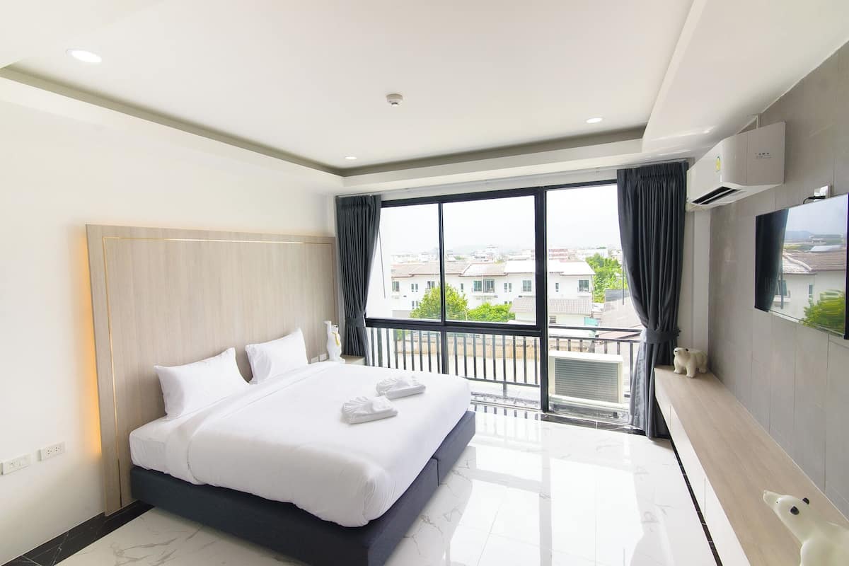 Une chambre d’hôtel moderne dotée d’un grand lit, d’un balcon avec vue et d’un téléviseur à écran plat fixé au mur.