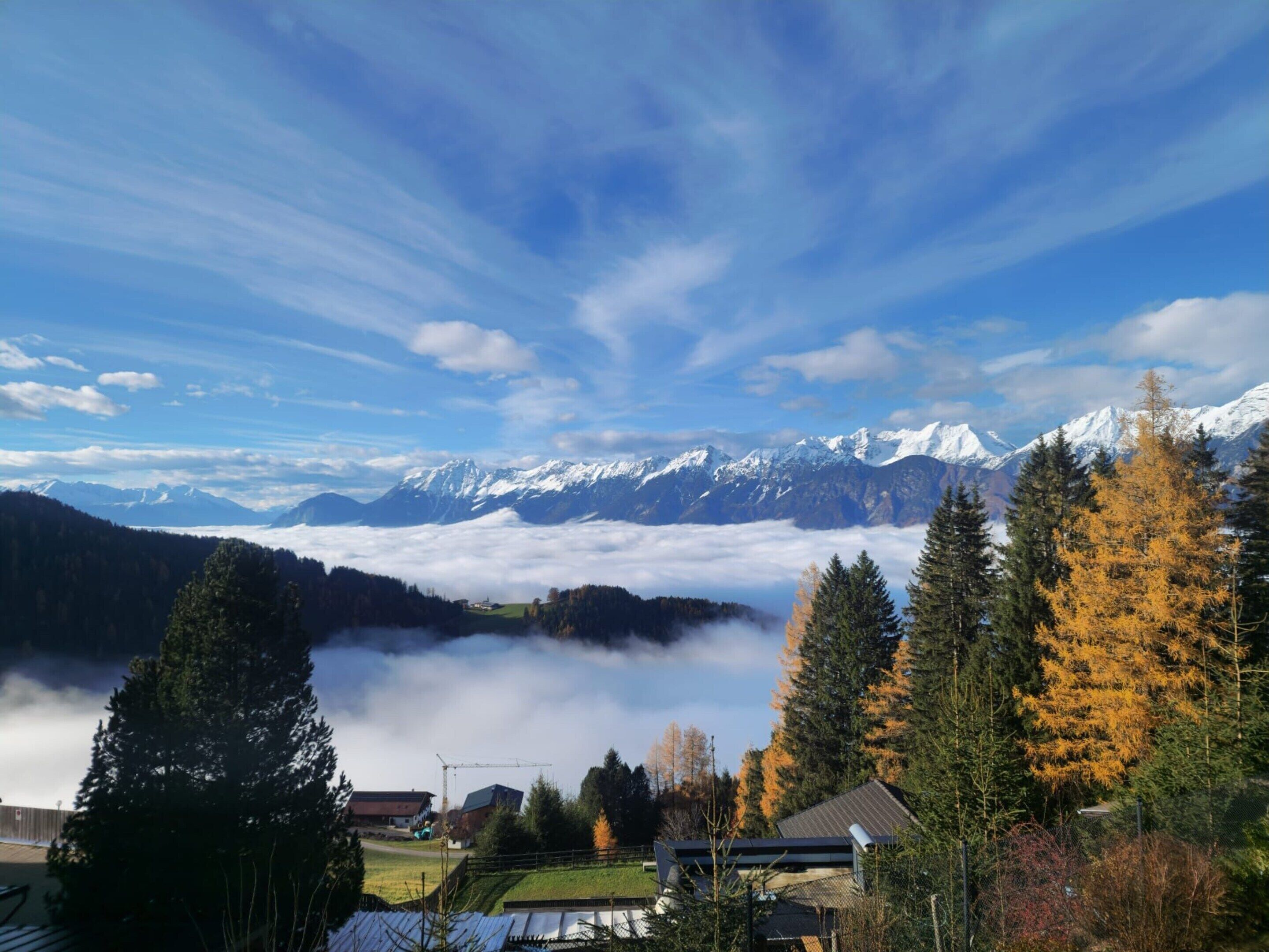 Eine gebirgige Landschaft mit schneebedeckten Gipfeln, einem bewaldeten Tal und einem kleinen Gebäude mit schrägem Dach.