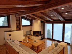 A cozy living room with a fireplace, wooden beams, a sofa, and a large window with a view of the mountains. - Amazing Cottage in Tyrol With Sauna (Volders)