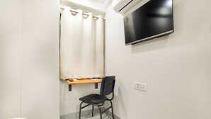 A bathroom with a shower curtain, a black chair, a mounted TV, and a small shelf with a mirror and a towel. - Aceotel Inn Xpress Vijay Nagar (Indore)